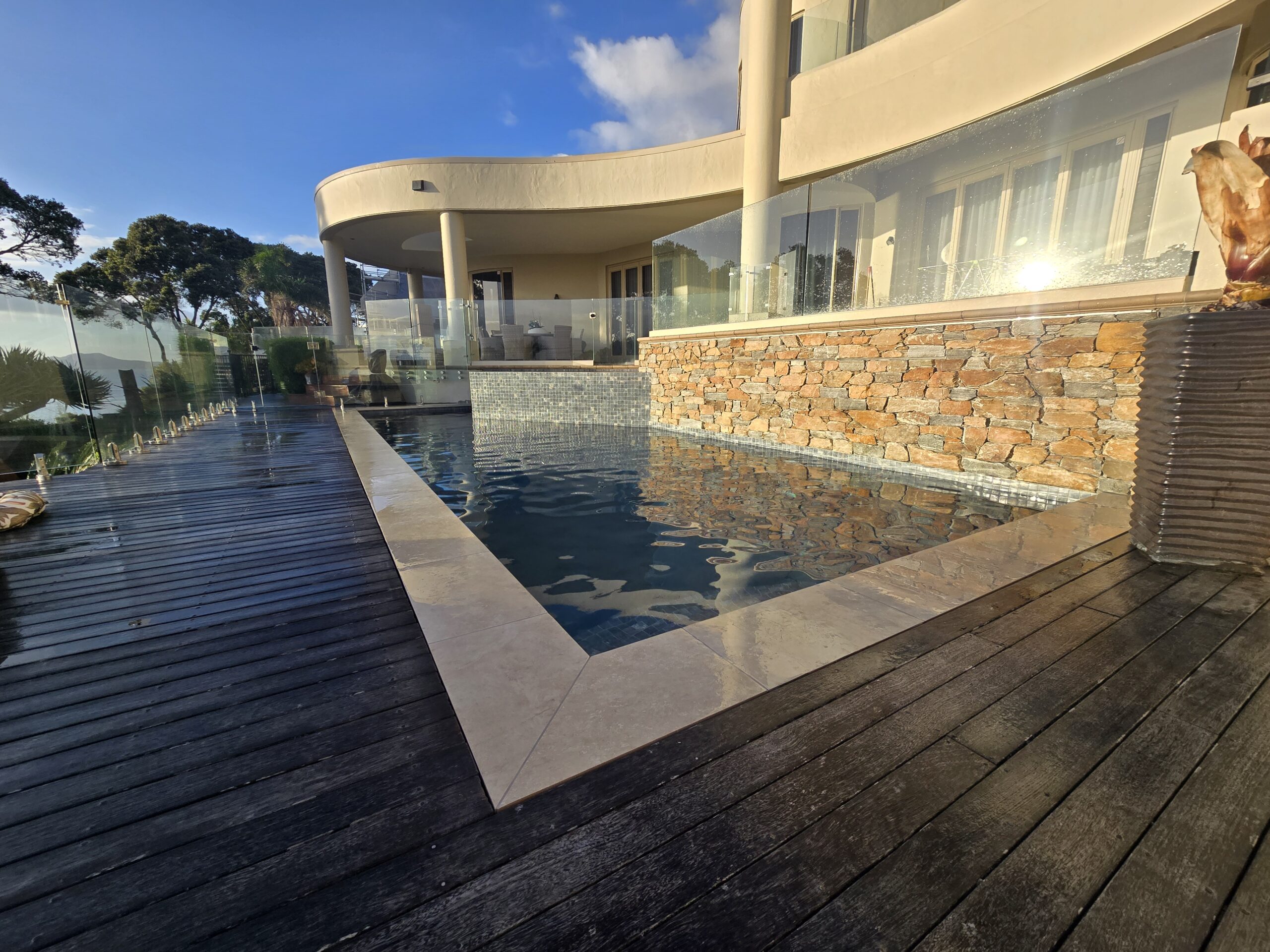 Natural schist stone feature wall beside a tiled pool in Waiake